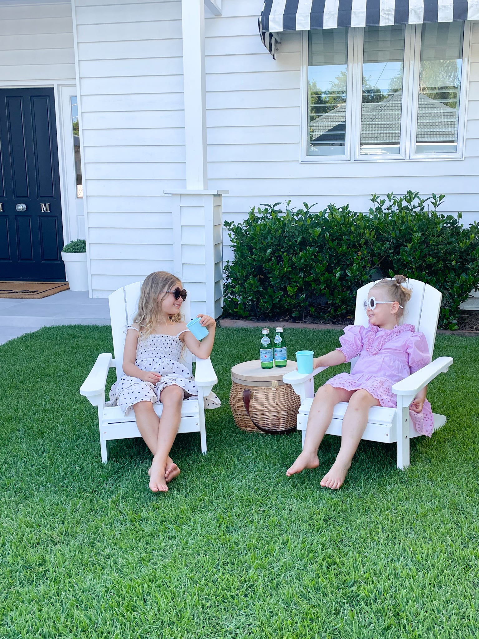 Two young girls sitting in the garden on white children's Adirondack Chairs
