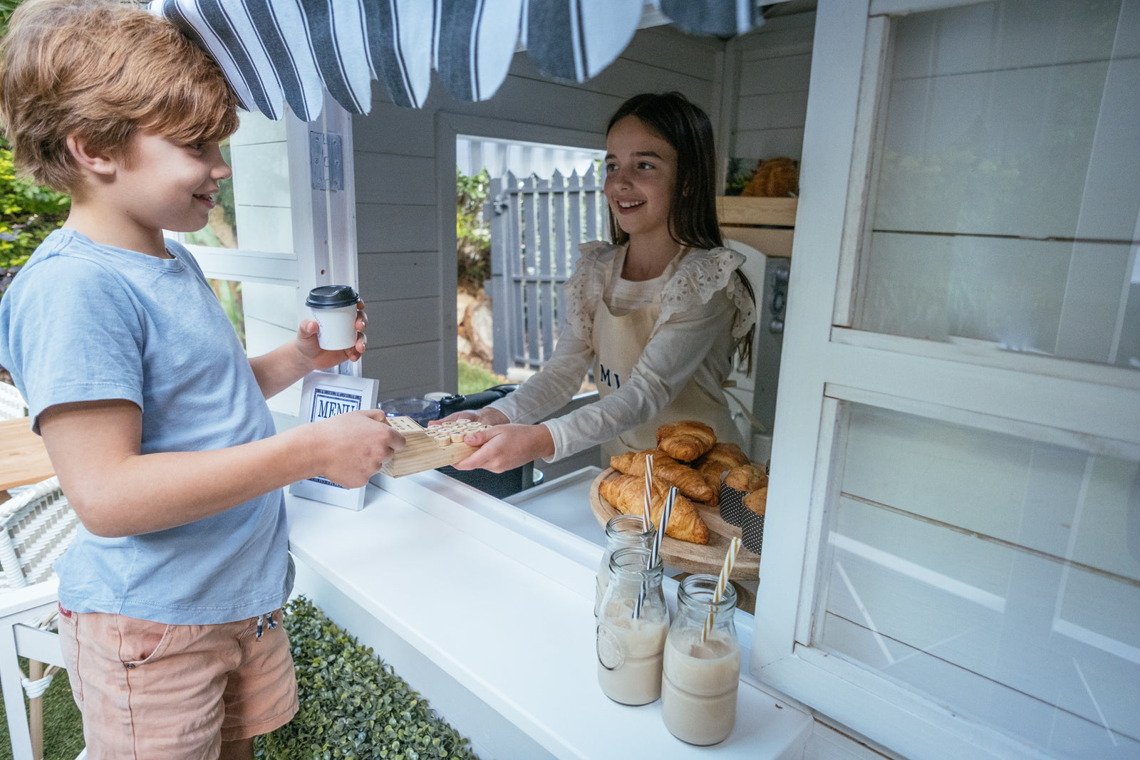 Young boy and girl play cafe in her white timber cubby house