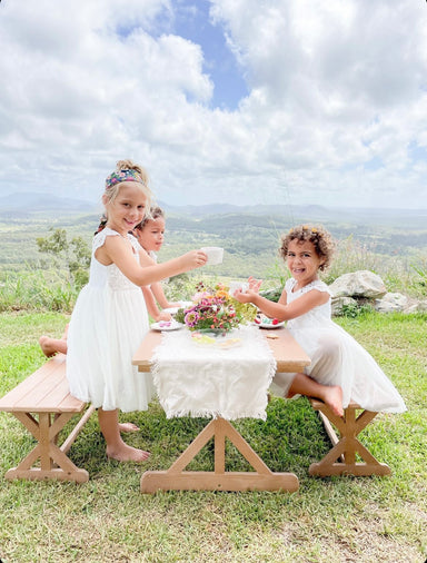 Young children in the garden having a tea party around a timber outdoor setting