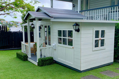 White timber garage attached to white cubby house with grey roof. The garage has one large front door and one side window.