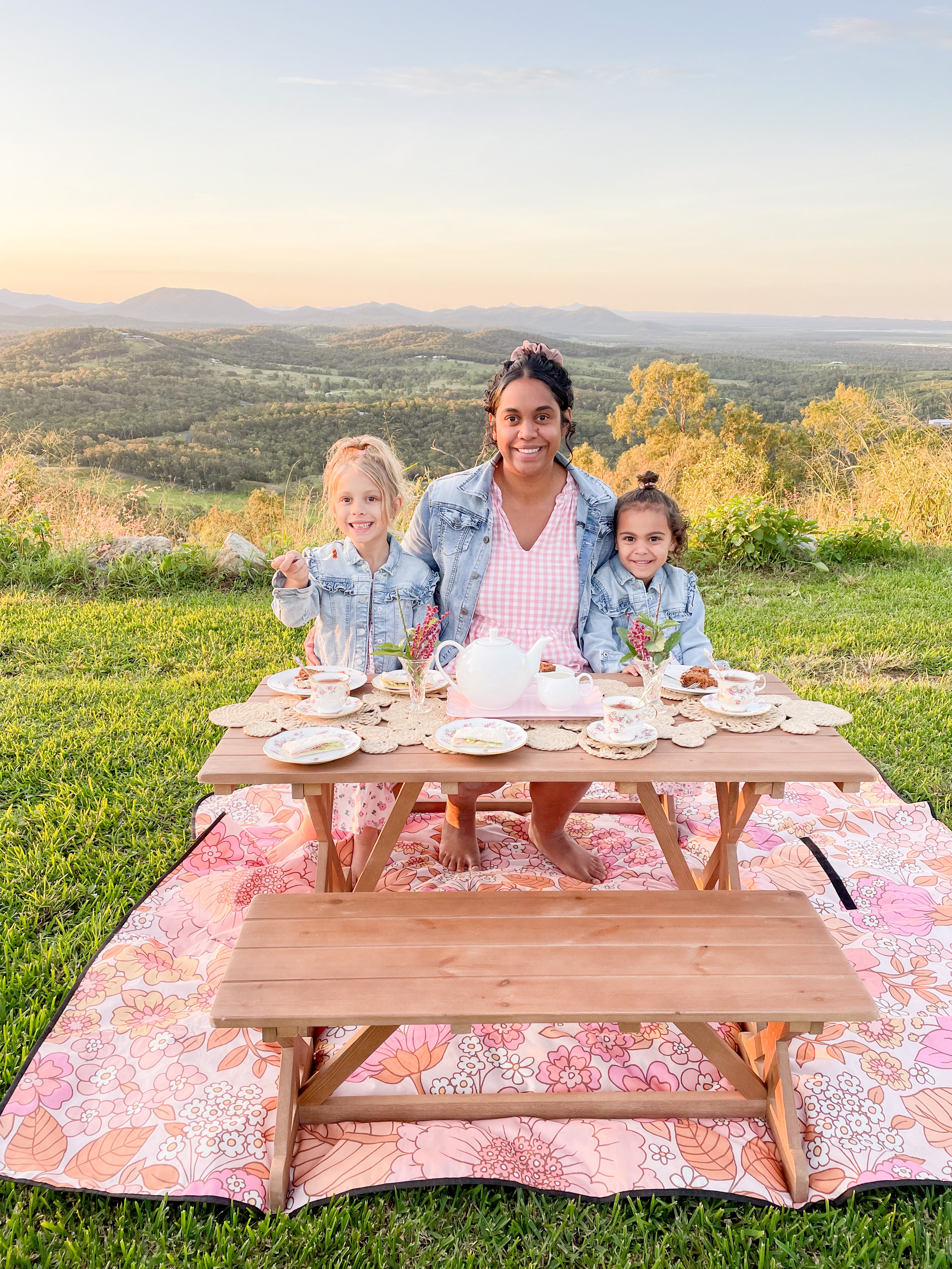 Mum and daughters sit outside in the garden on My Little Manor Outdoor Bench Seat Set