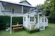 Large white and grey timber cubby house. Pergola and garage attached. Kids outdoor furniture is displayed
