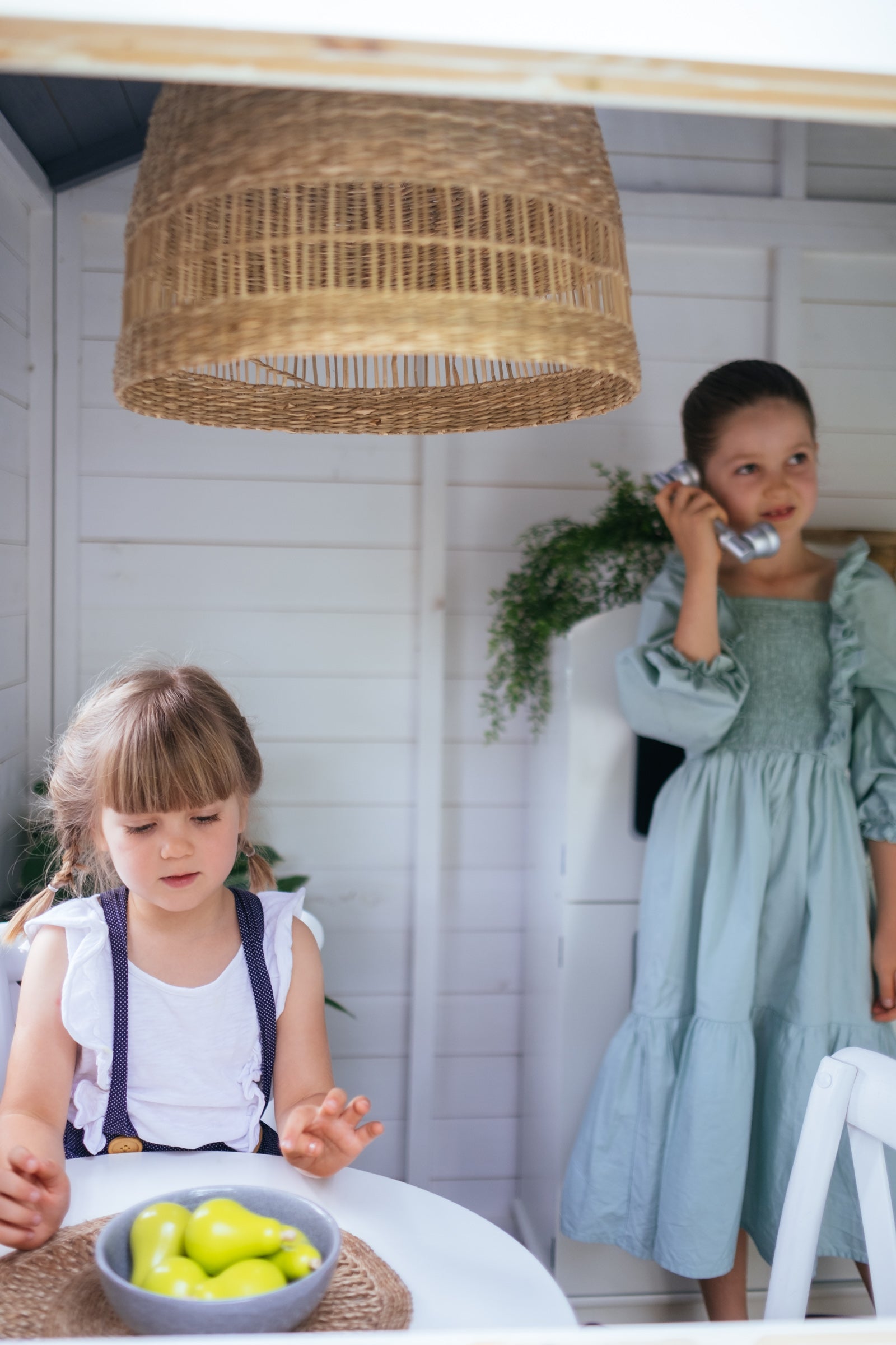 Young girls play inside white timber cubby house. 