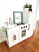 Children's Hamptons shaker style white play kitchen with gold fixtures and decorated with easter decorations. White toy kitchen